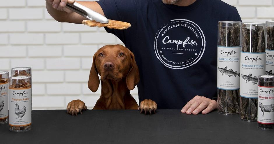 A person hands a natural dog treat to a patient dog.