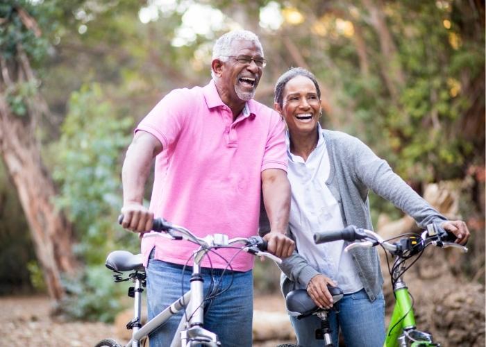 A senior couple laugh while biking through a park